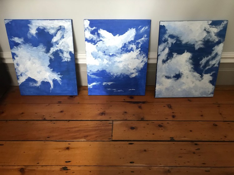 Three paintings by Ciorsdan Glass showing blue sky and clouds in different shapes.